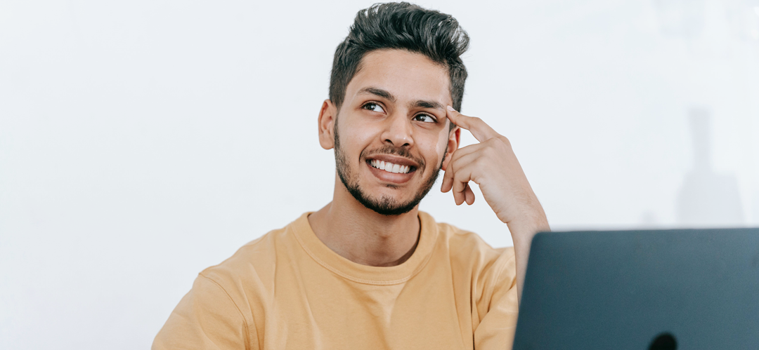 De la recherche à l’ouverture de sa franchise — étapes clés du parcours Jeune entrepreneur souriant devant son ordinateur, dans la phase de recherche et de préparation à l'ouverture de sa franchise